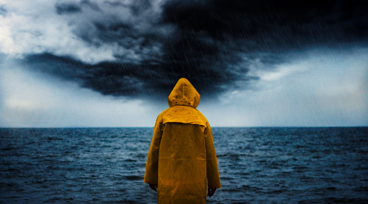 Person standing at the edge of the sea watching a storm roll in
