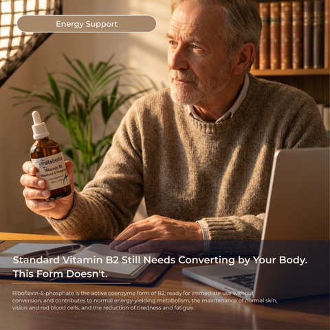 Man holding a bottle of Vitamin B2 with a laptop, sitting at a desk.